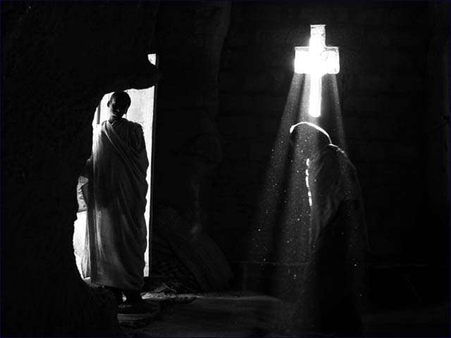 A ray of light penetrates from a cross-shaped window into the rock-hewn church of Bet Merkorios in Lalibela as an Ethiopian pilgrim walks by.