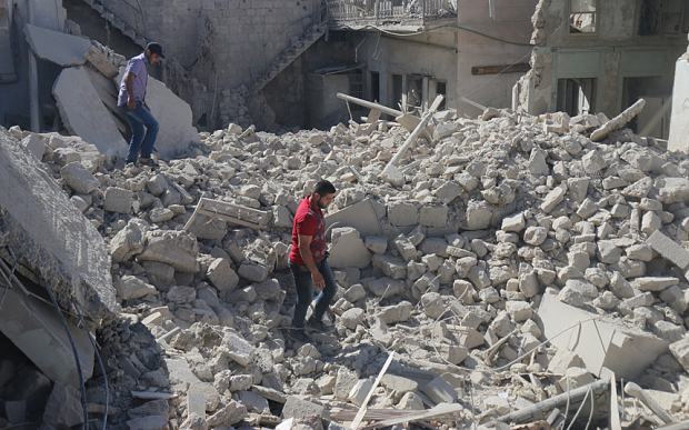 Residents walk amidst rubble at a site allegedly hit by a barrel bomb in Aleppo