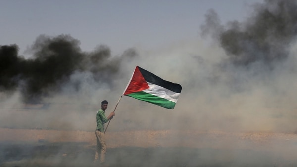 Un manifestante palestino sostiene su bandera en medio del humo