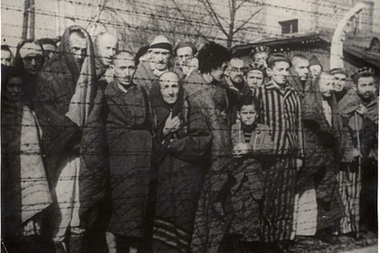 Sobrevivientes del Holocausto detrás de una cerca de alambre de púas tras su liberación del campo de exterminio nazi de Auschwitz-Birkenau en 1945, en la Polonia (Archivos de Yad Vashem/Reuters)