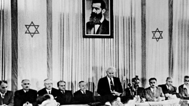 Le premier premier ministre d'Israël, David Ben-Gourion, sous un portrait de Theodor Herzl, fondateur du sionisme, déclare l'indépendance d'Israël.