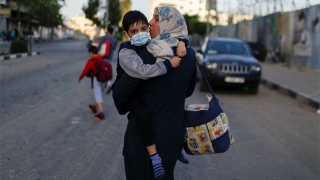 Una mujer palestina junto a su hijo evacúa su edificio después de que fuera impactado por un ataque aéreo israelita el 12 de mayo de 2021.