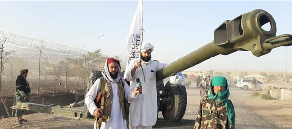 Partidario sostiene en alto la bandera de los talibanes afganos junto al arsenal incautado.