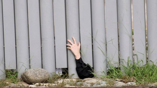Un niño saca su mano por debajo de una cerca a manera de protesta.